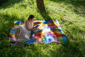 A beautiful middle-aged woman rests and reads a book, lying in the middle of a field on a colorful...