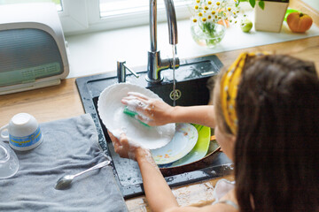 Getting chores done quicker together. Cropped shot of little daughter washing dishes together at...