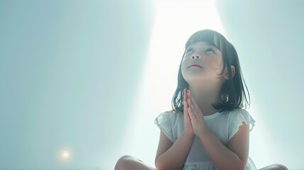 Mała dziewczynka, siedząca na podłodze na jasnym tle, modli się z zamkniętymi oczami i złożonymi dłońmi