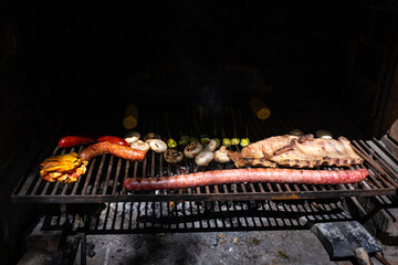 Some beef and pork sausages are cooked on a barbecue with some vegetables. Sausages, chorizo, and...