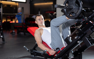 Young athletic man in sportswear training her legs with barbell in gym