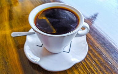 White cup of black Americano coffee on a wooden table.