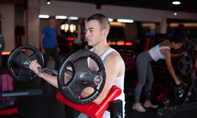 Young athletic man lifting heavy barbell in gym