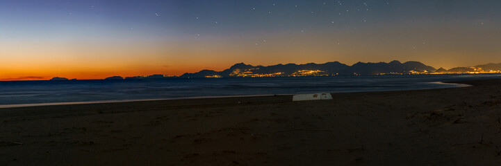 Panorama of sandy beach with white boat and illuminated Amalfi Coast during evening twilight after...