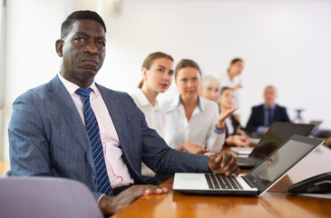 African-american businessman using laptop during conference in meeting room. Man sitting at desk with colleaugues.