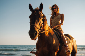 Portrait of the girl galloping on a horse on an ocean coast during a sunset