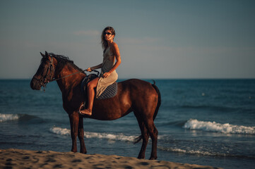 Side view of an attractive woman riding a horse on a beach during a dusk
