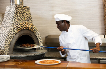 Emotional African American man chef having problems while preparing pizza in restaurant, taking...