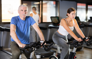 Elderly athletic man in sportswear training on exercise bike in gym