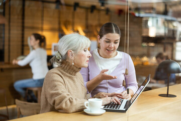 Two women discussing something on a laptop screen while sitting at the bar in a restaurant