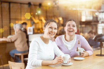 Two happy women drinking coffee and talking in quiet cafe
