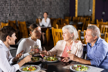 Elderly couple and young couple chatting and enjoying dinner in restaurant