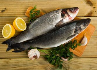 Raw sea basses with lemon, parsley, garlic and spices on cutting board on wooden background