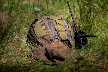 Helmet, walkie talkie and tactical gloves on the ground on a sunny day. Military equipment,...