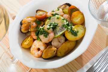Close up of tasty warm salad with fried potatoes, shrimp and mussels, served at plate