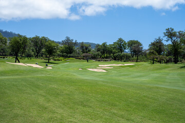 Scenic view of golf course, fairway leading up to golf green protected by sand traps, tropical landscape, vacation recreation on Hawaii
