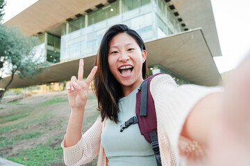 Happy asian female teenage student laughing and shooting a selfie with a cellphone. Young chinese...