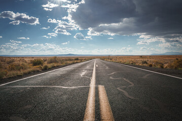 Scenic desert road in Arizona two lane path surrounded by golden grasslands under dramatic skies with hints of rain. Characteristic of Southwest USA.