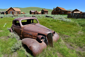 Beneath the clear blue summer sky, a rusting car sits in Bodie, California.

