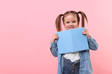 Cute little girl with book on pink background. Space for text