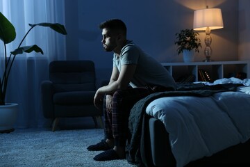 Frustrated man sitting on bed at night