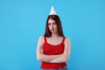 Sad woman in party hat on light blue background