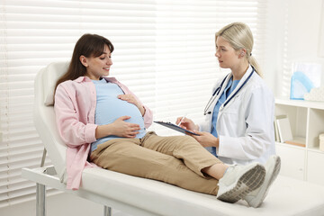 Doctor with clipboard consulting smiling pregnant patient in clinic