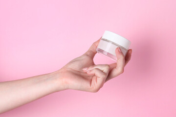 Woman holding jar of cream on pink background, closeup