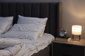 Nightlight, alarm clock and book on bedside table near bed indoors