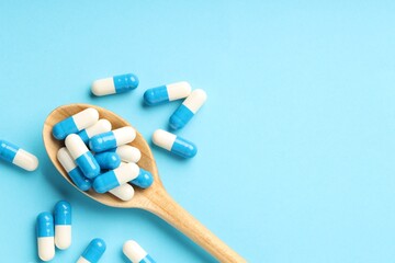 Many antibiotic pills with wooden spoon and space for text on light blue background, top view. Medicinal treatment