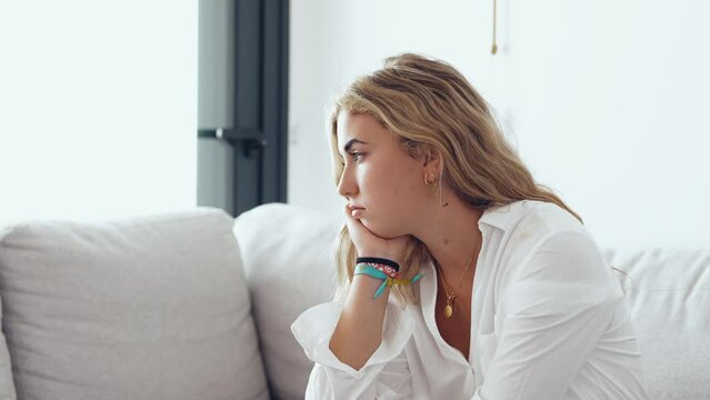 Side view young woman looking away at window sitting on couch at home. Frustrated confused female feels unhappy problem in personal life quarrel break up with boyfriend or unexpected pregnancy concept