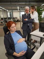 Elderly Caucasian man and woman gossiping behind their sleeping pregnant colleague in the office....