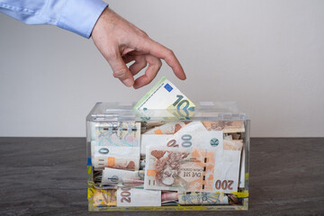 giving Charity in nominal 100 Euro banknotes to a transparent donation box for money donation. A financial support, collects money. The act of giving supports charitable initiatives