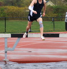 Runner puching off the steeplchase barrier over the water pit