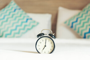 Hotel bedroom alarm clock on bed home interior cozy decoration room. Clean soft white bedsheet stylish decor relax dorm copy space. Alarm clock black vintage retro time white light Blurred background