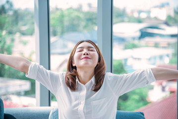 Relax woman yawning sitting on cozy sofa in apartment. Asian woman relax stretching arm laziness comfortable in living room. Happiness girl lifestyles sitting at home living room. Stretching arm relax