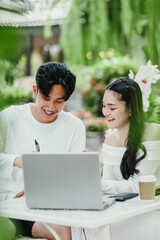 Happy couple is collaboratively engaged in work on a laptop at a white table, enjoying their time together in a lush garden setting.