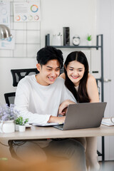 Cheerful young couple works together on a project, sharing a light moment in front of a laptop in their well-organized home office.