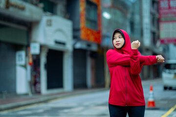 Glad smiling young asian muslim female in hijab with fitness tracker running on building background...