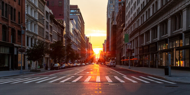 Empty streets and sidewalks at 5th Avenue and 23rd St in New York City with sunset shining between the background buildings of the Manhattan cityscape