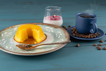 Small quindim, traditional Brazilian sweet, next to a spoon, coffee cup and a candle_3.