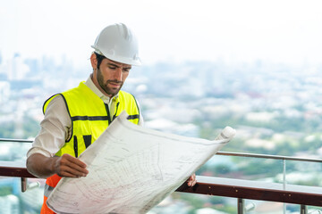 Male civil engineer contractor in safety helmet and jacket standing on construction site building...