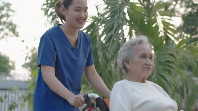 Young nurse and elderly asian senior woman on wheelchair, Asian careful caregiver and patient,  Nurse gives a pep talk to an elderly female patient in the garden in the evening. Health insurance.