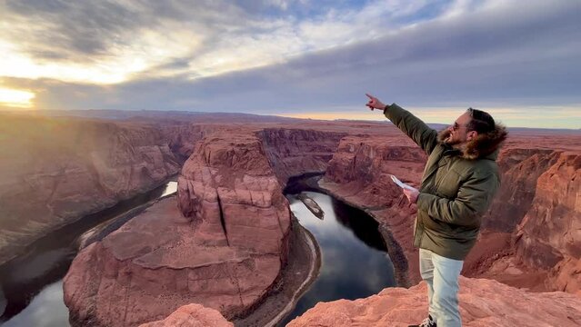Young traveler male enjoying his solo own vacation time on top of Horseshoe Bend while looking the horizon checking on a map the landscape of Glen Grand Canyon National Park in Arizona, USA.