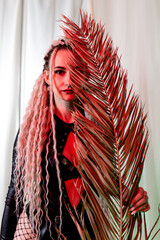 Portrait of a beautiful girl with dreadlocks. Go-go dancer in sexy black leather posing with dry palm leaves. red backlight