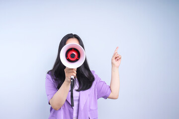Woman shouting and holding megaphone while pointing to the side on grey background