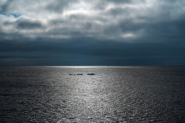 2023-12-31 THREE SMALL ICE CHUNKS FLOATING IN THE ARCTIC OCEAN WITH A CLOUDY SKY AND A REFLECTION...