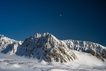 2023-13-31 SNOW COVERED JAGGED PEAKS WITH A BLUE SKY AND A MOON NEAR SVALBARD NORWAY IN THE ARCTIC