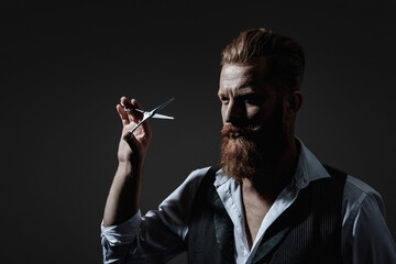 Handsome barber using scissors while cutting hair. Modern barbershop haircut. Bearded hipster...
