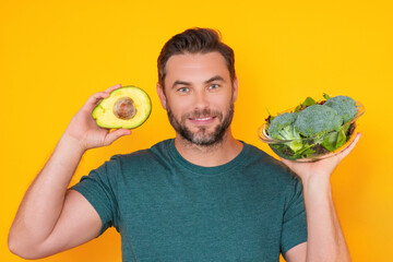 Man hold avocado, isolated on yellow. Man holding avocado and broccoli vegetables. Cooking avocado....